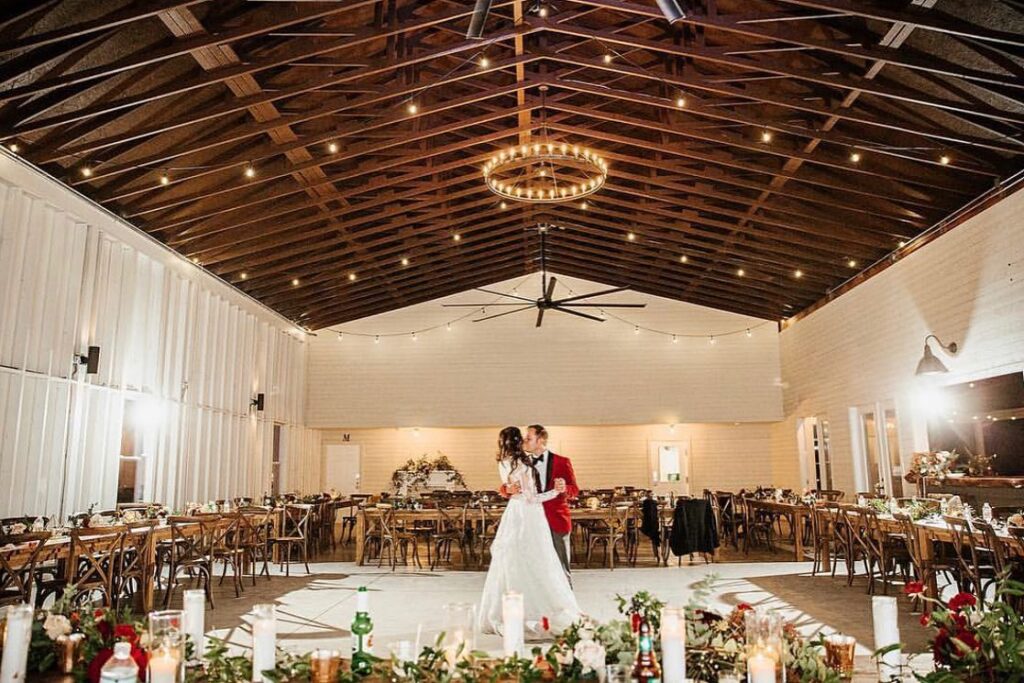 bride and groom dancing in modern barn wedding reception under chandelier at christmas wedding